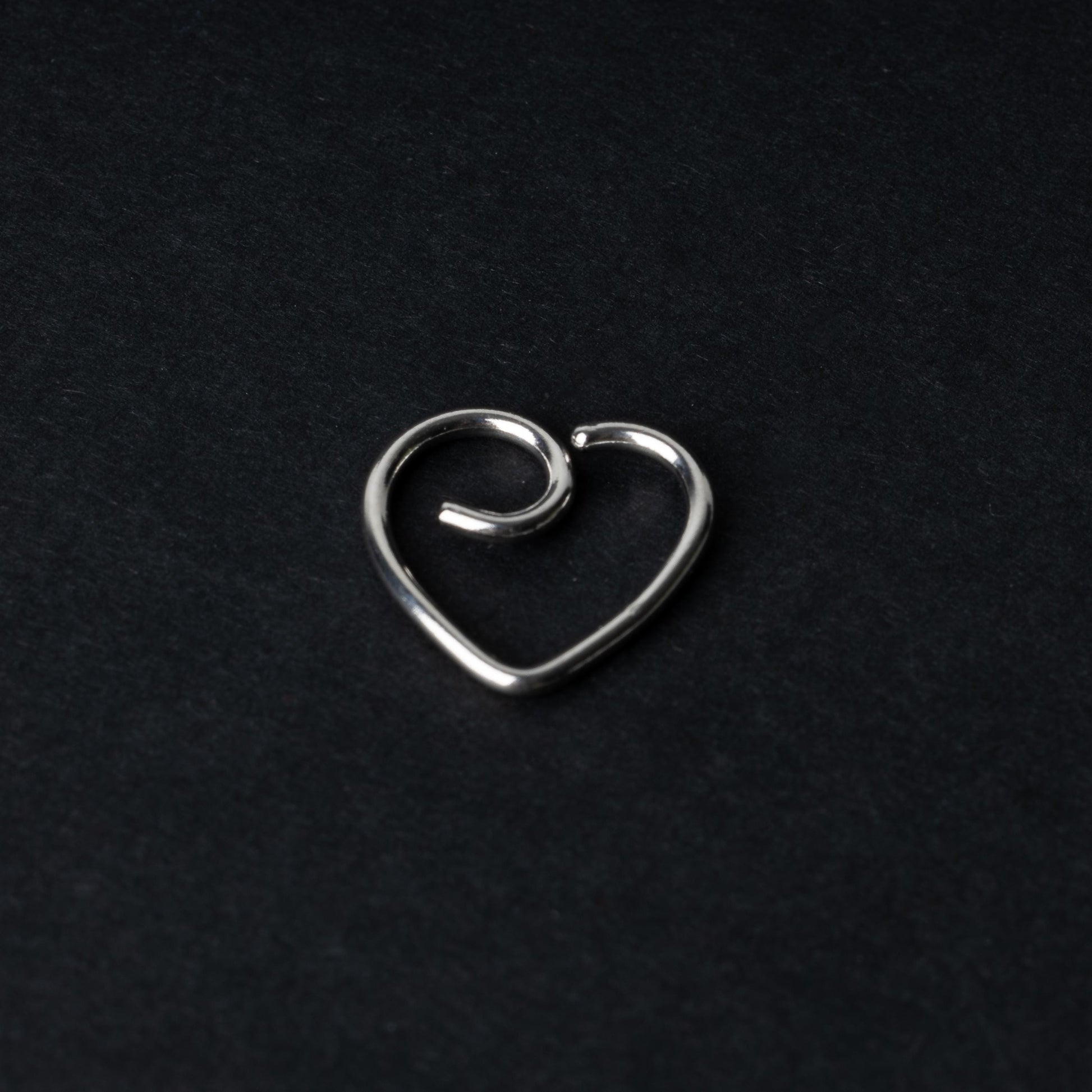 Silver heart shaped daith on a dark background