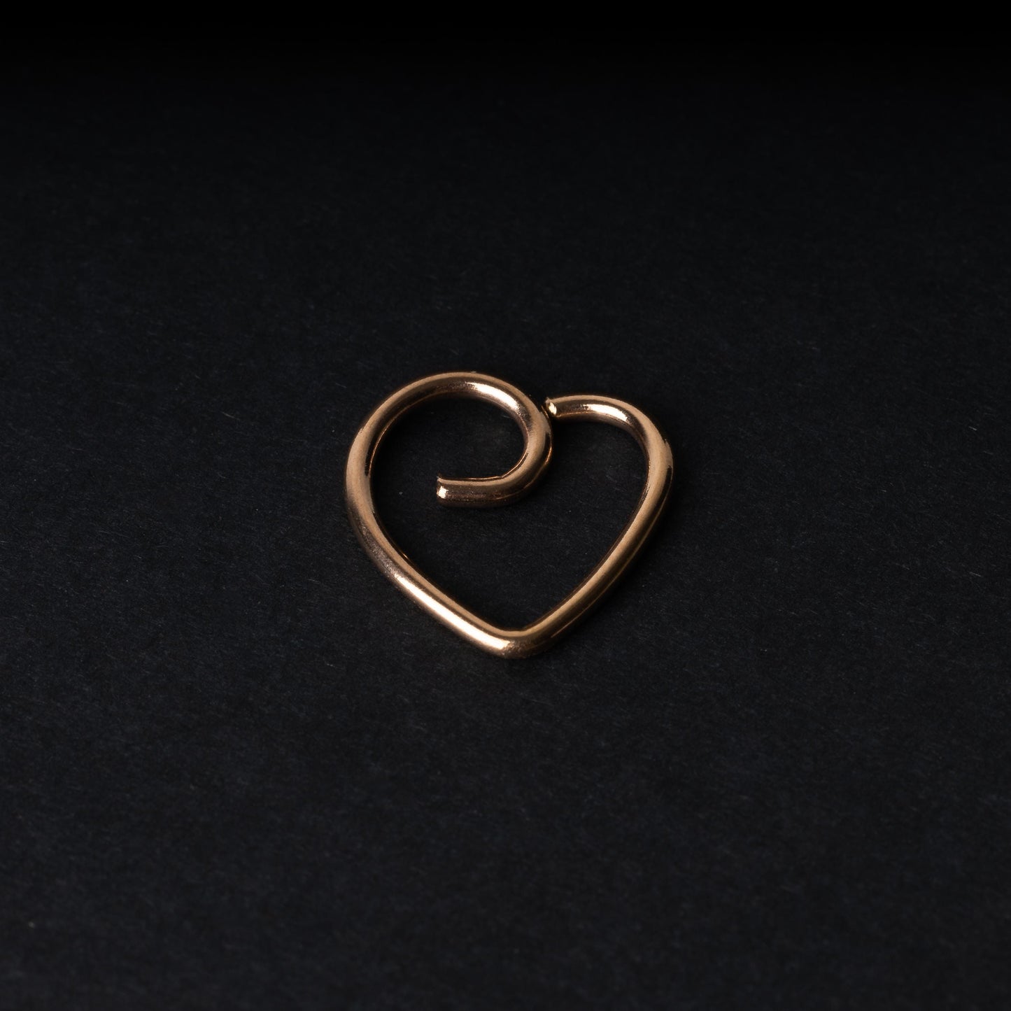 Rose gold heart shaped daith on a dark background