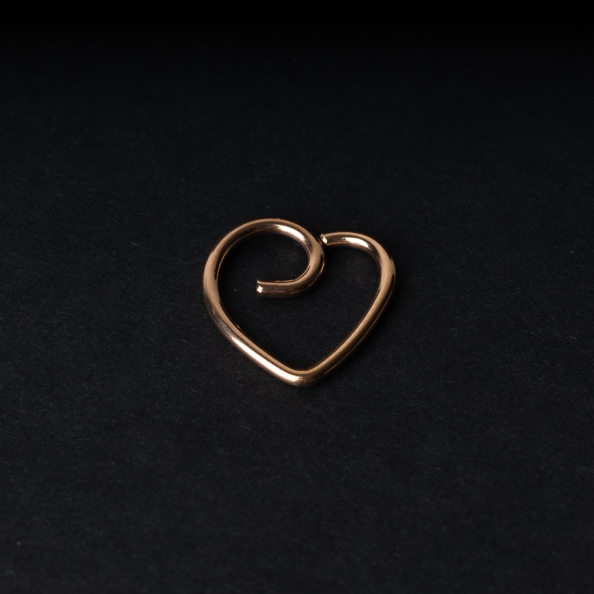 Rose gold heart shaped daith on a dark background