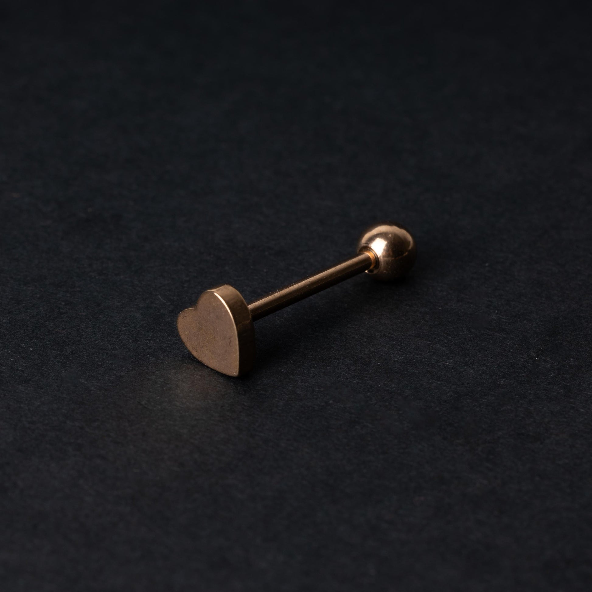 Heart shaped tongue bar in rose gold, displayed on a dark background.