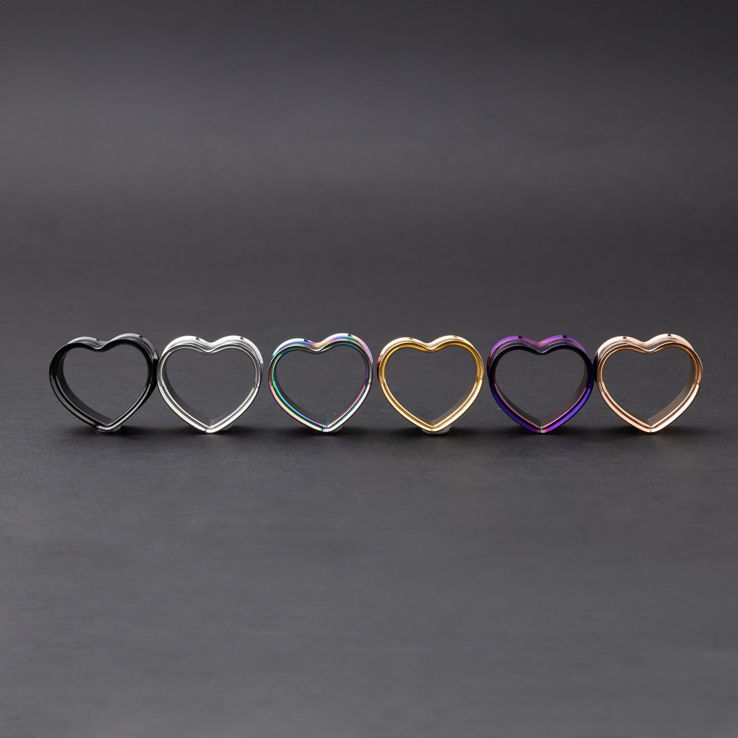 Heart-shaped tunnels in black, silver, rainbow, gold, purple, and rose gold finishes, displayed on a dark background.