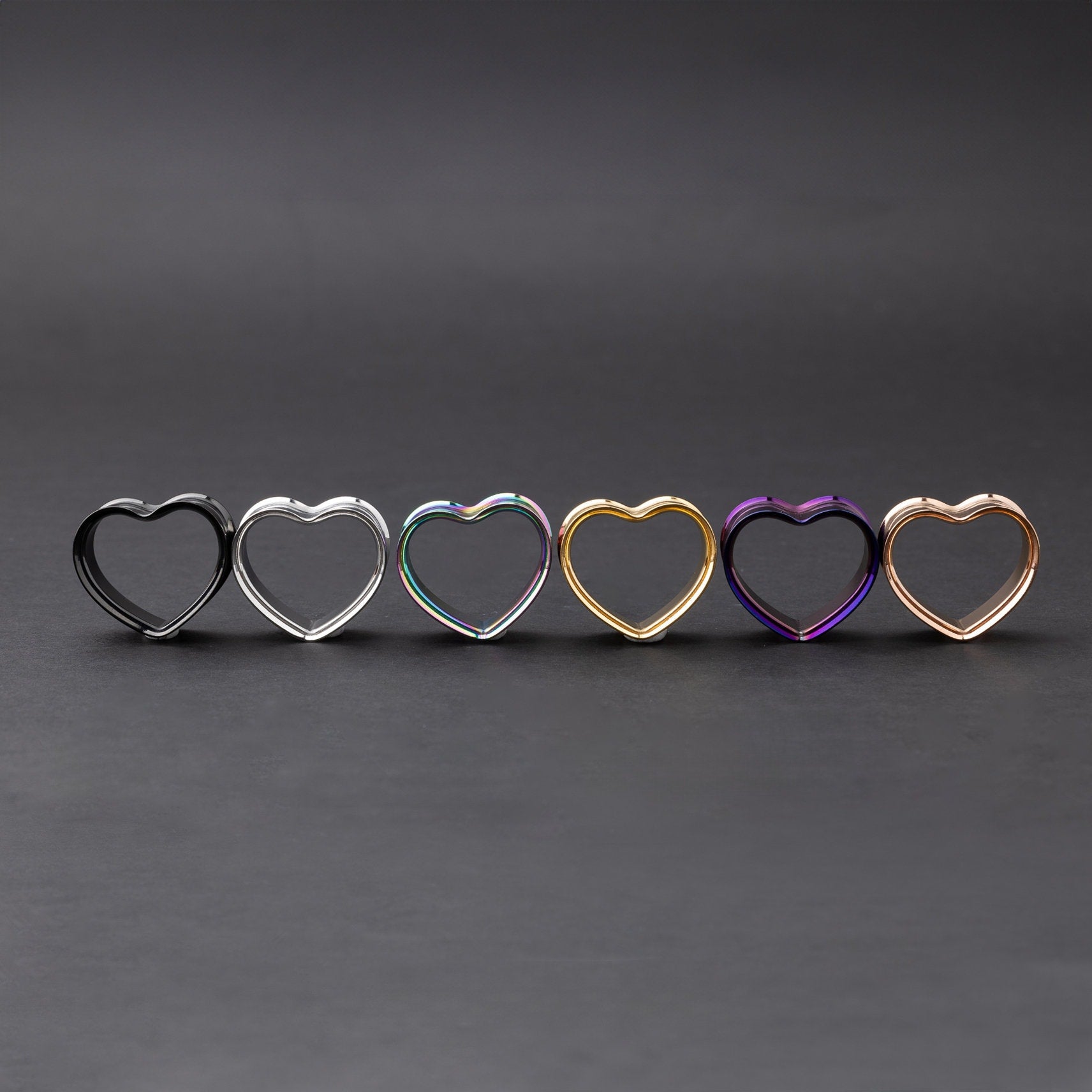 Heart-shaped tunnels in black, silver, rainbow, gold, purple, and rose gold finishes, displayed on a dark background.