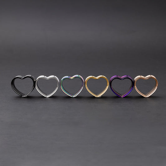 Heart-shaped tunnels in black, silver, rainbow, gold, purple, and rose gold finishes, displayed on a dark background.