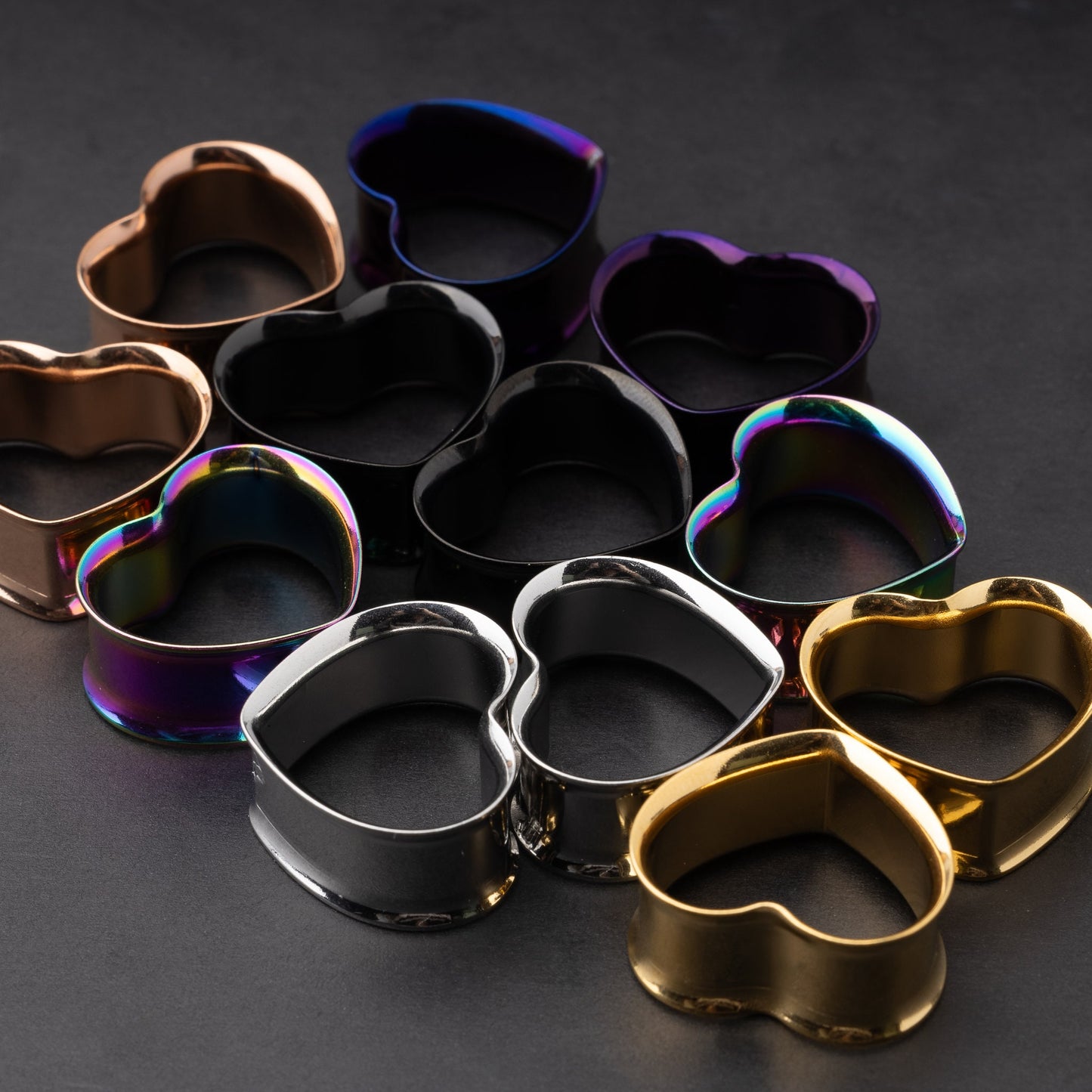 Heart-shaped tunnels in black, silver, rainbow, gold, purple, and rose gold finishes, displayed on a dark background.