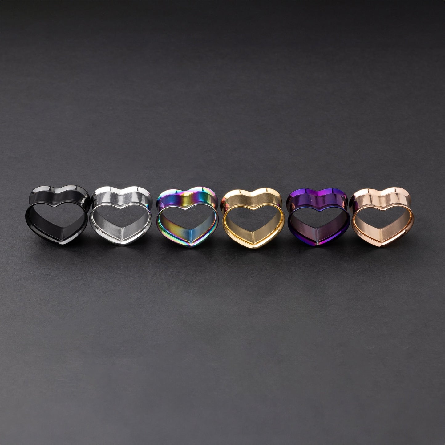 Heart-shaped tunnels in black, silver, rainbow, gold, purple, and rose gold finishes, displayed on a dark background.