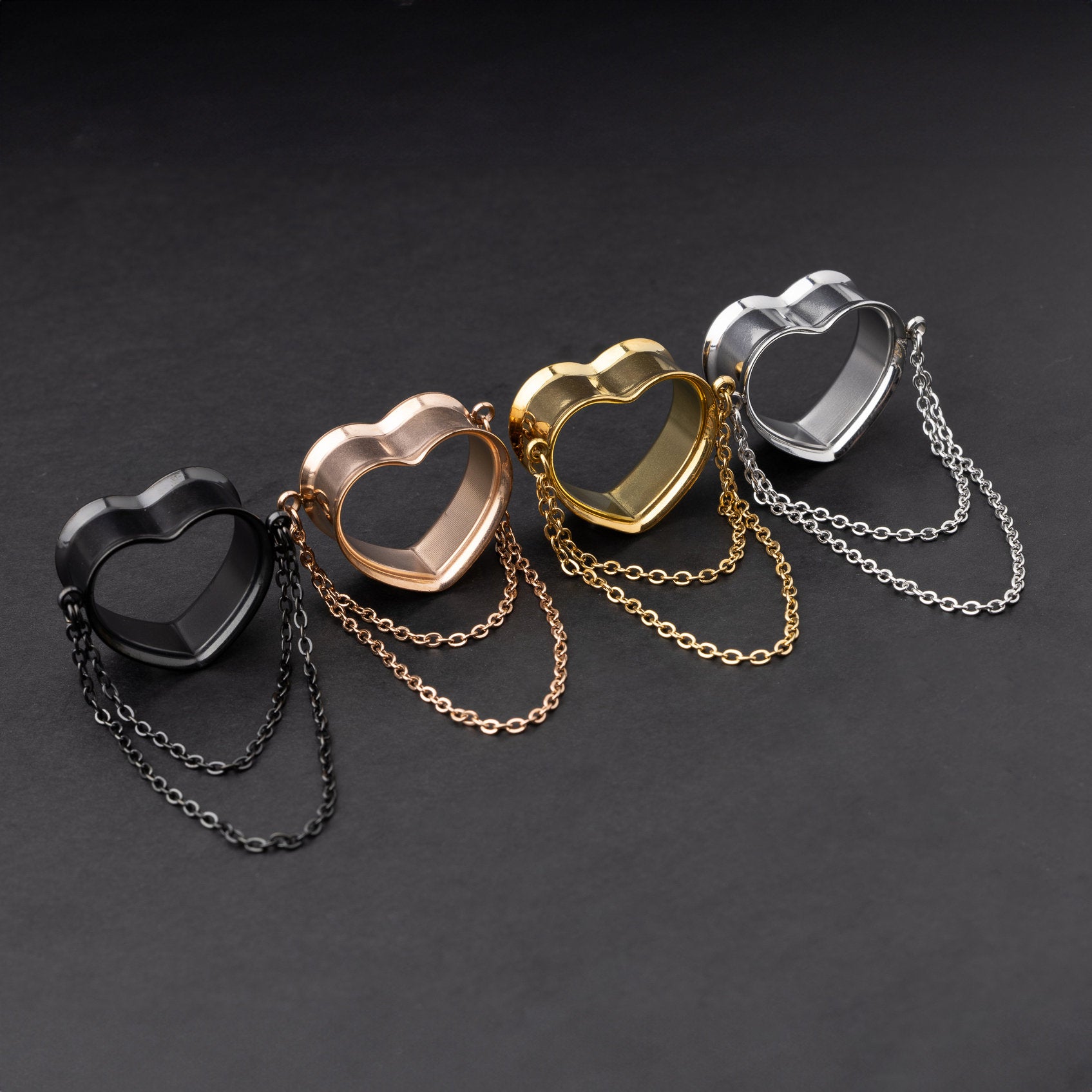Heart-shaped tunnels with draped chains in black, rose gold, gold, and silver finishes, displayed on a dark background.
