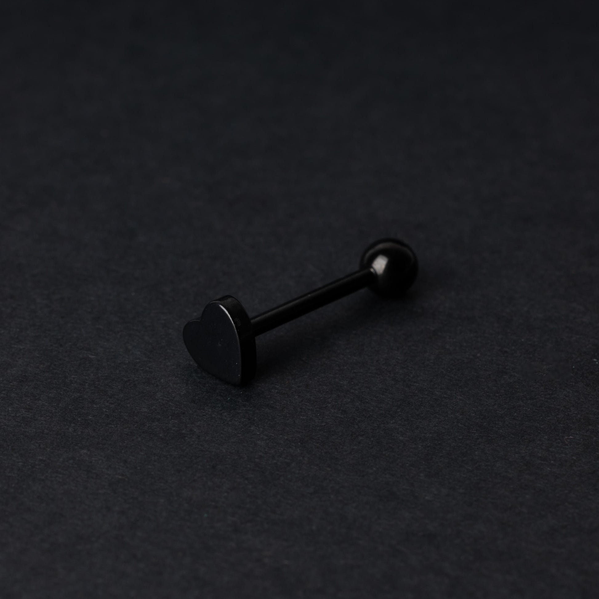 Heart shaped tongue bar in black, displayed on a dark background.