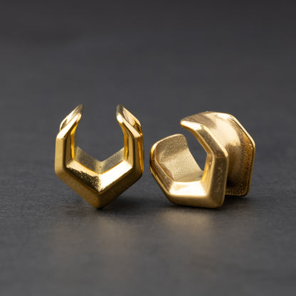 Gold geometric chevron-shaped ear cuffs displayed on a dark background.