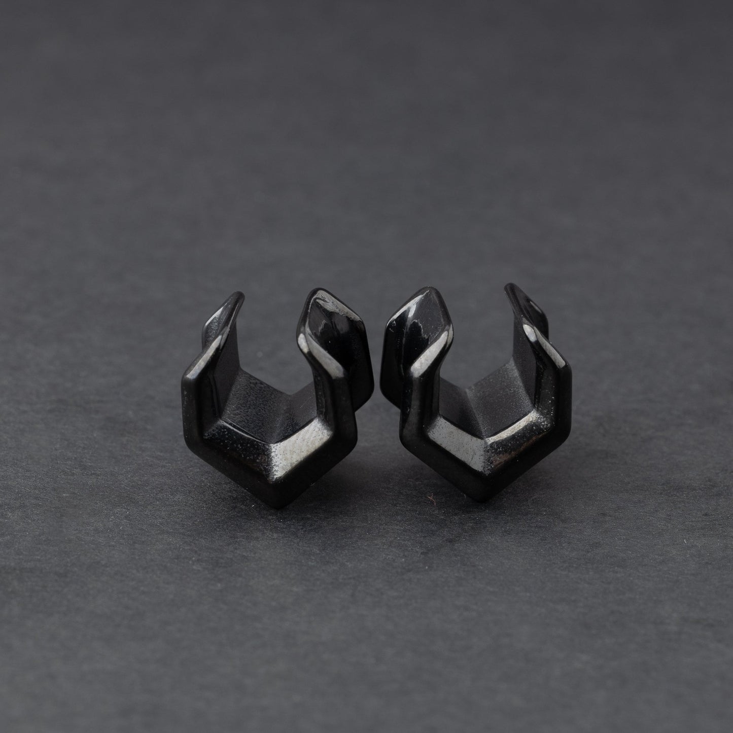 Black geometric chevron-shaped ear cuffs displayed on a dark background.