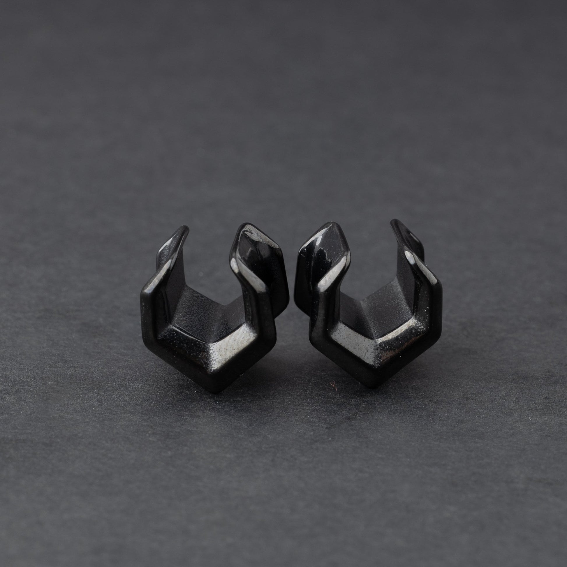 Black geometric chevron-shaped ear cuffs displayed on a dark background.