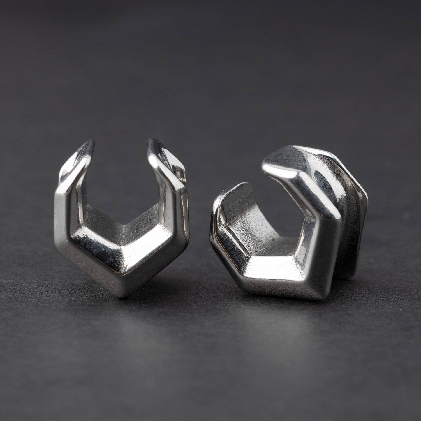 Silver geometric chevron-shaped ear cuffs displayed on a dark background
