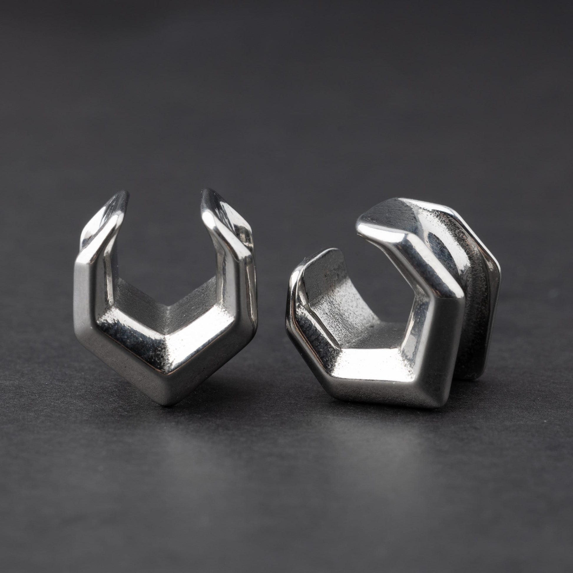 Silver geometric chevron-shaped ear cuffs displayed on a dark background