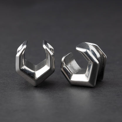 Silver geometric chevron-shaped ear cuffs displayed on a dark background