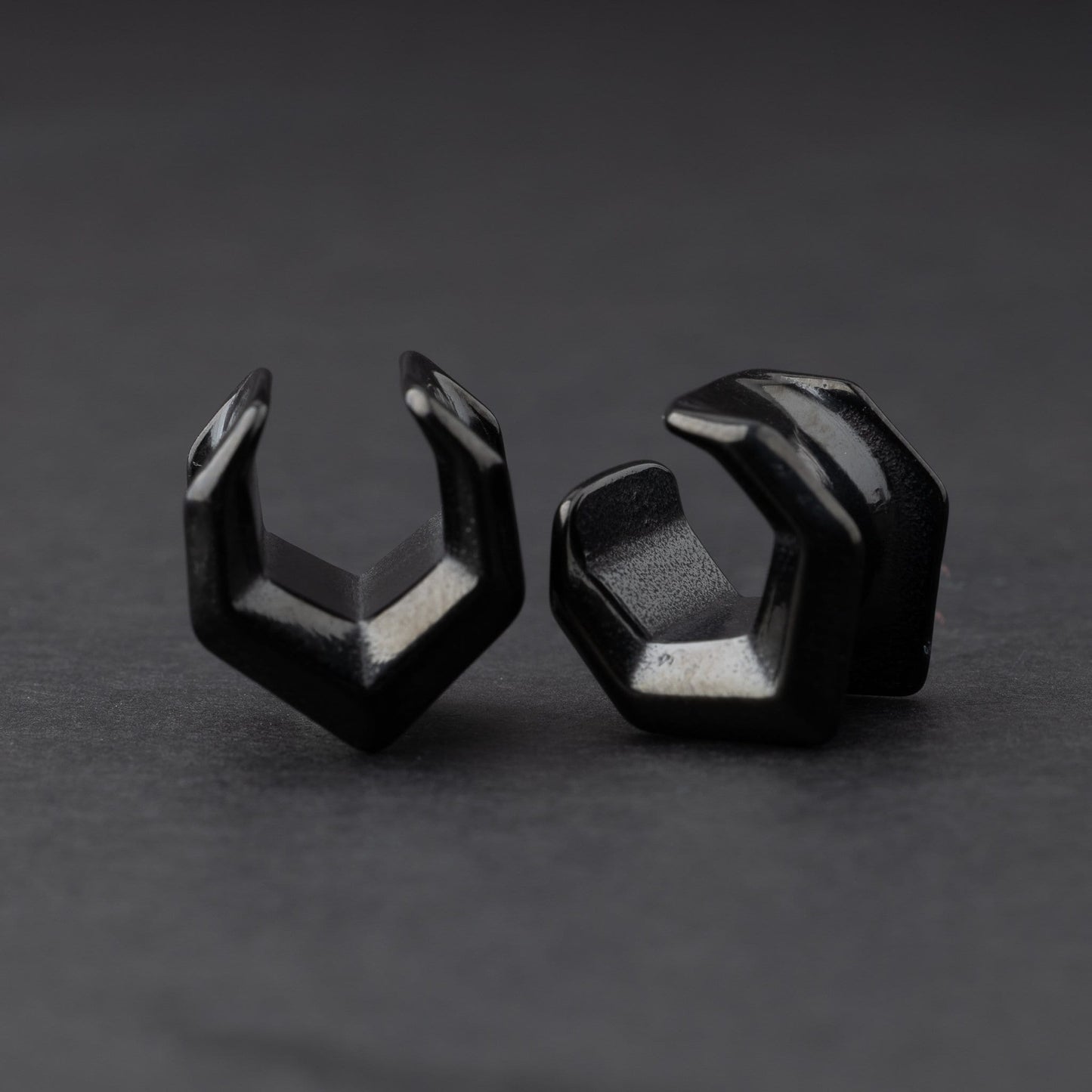 Black geometric chevron-shaped ear cuffs displayed on a dark background.