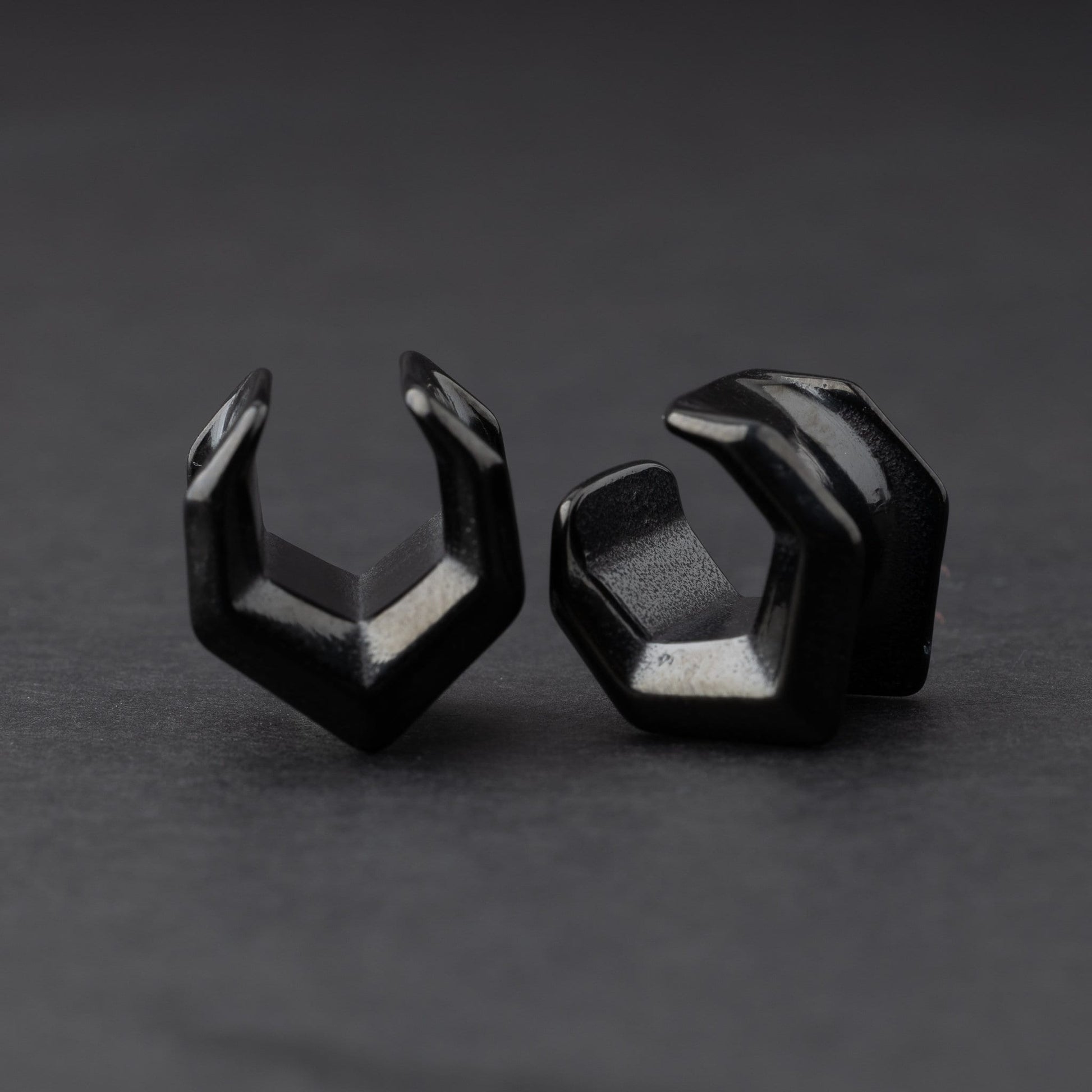 Black geometric chevron-shaped ear cuffs displayed on a dark background.
