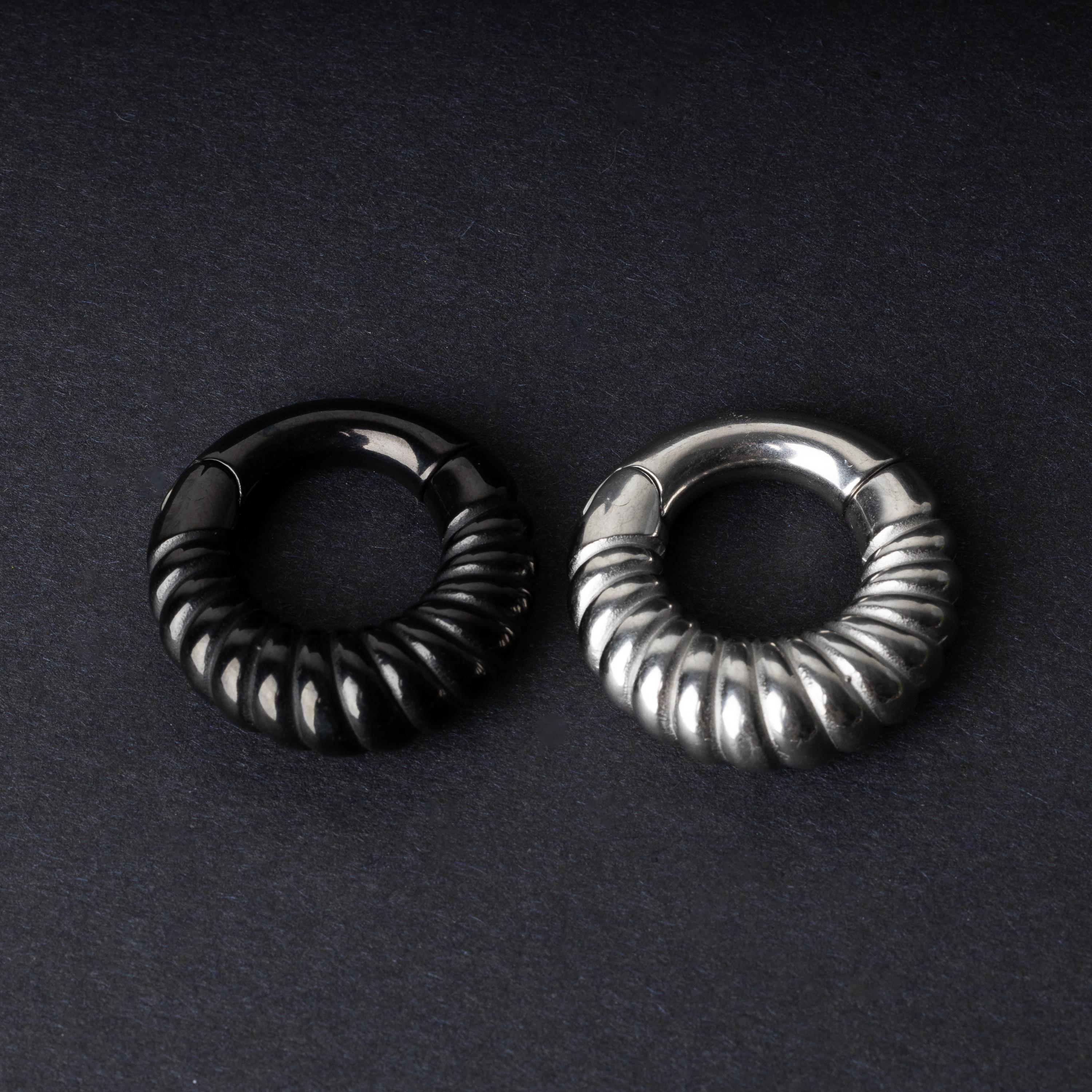 Two textured hoop rings with a ridged design, one in black and one in silver, displayed side by side on a dark background.