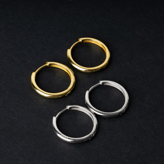 Two pairs of huggie hoop earrings, one in gold and one in silver, displayed on a black background.