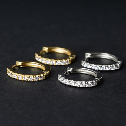 Two pairs of hoop earrings, one silver and one gold adorned with a row of sparkling cubic zirconia gems, displayed on a black background.