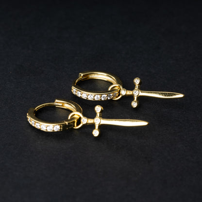 Gold-plated hoop earrings with crystal detailing and sword-shaped charms, displayed on a dark background.