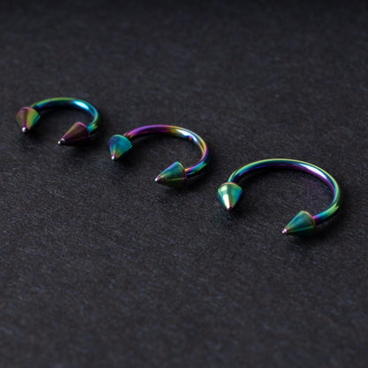 Three stainless steel horseshoe hoops with cone-shaped ends and a rainbow anodized finish displayed on a dark background, showcasing their bold design and vibrant colors.