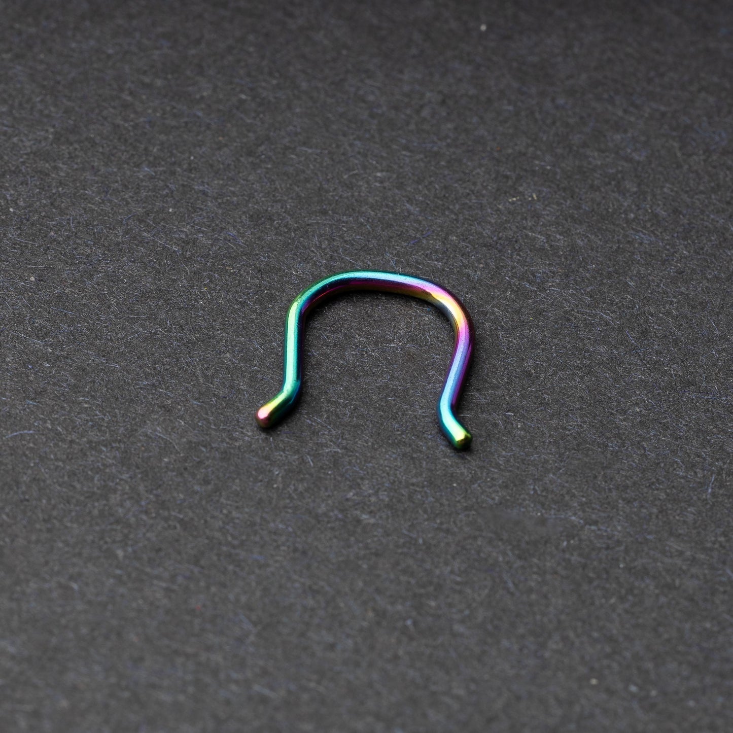 U-shaped septum retainer in rainbow displayed on a dark background