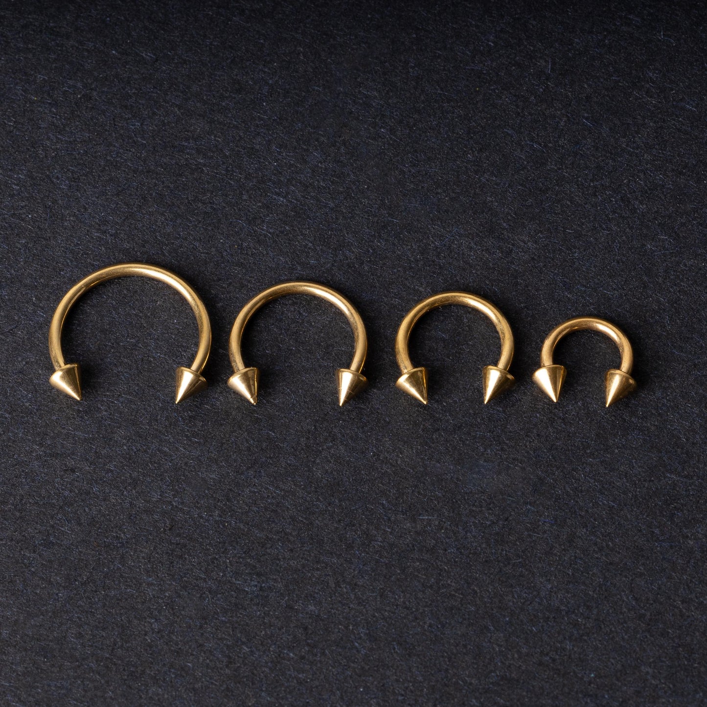 Various sized gold titanium circular barbells with spiked ends displayed on a dark background, arranged by size from large to small.