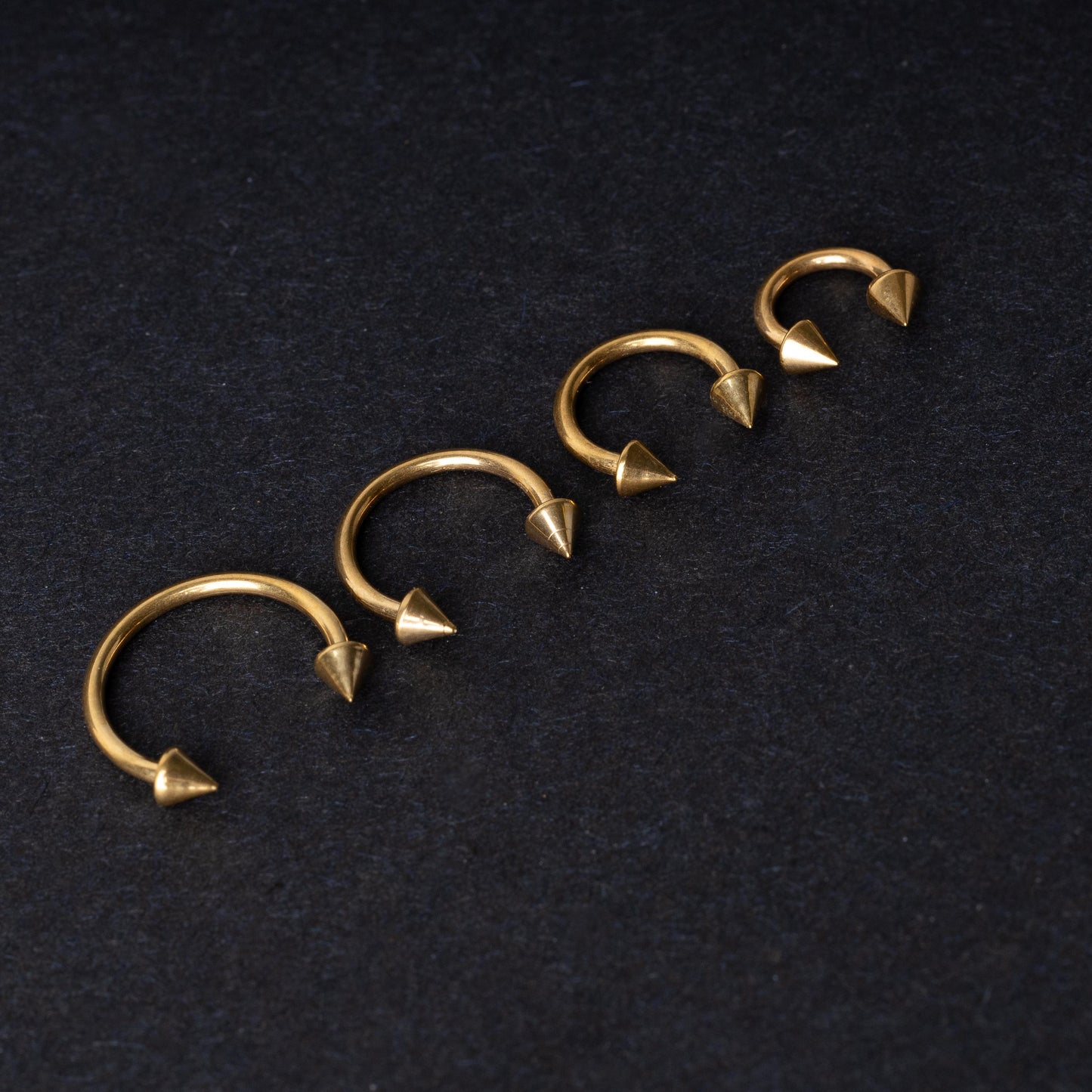 Various sized gold titanium circular barbells with spiked ends displayed on a dark background, arranged by size from large to small.