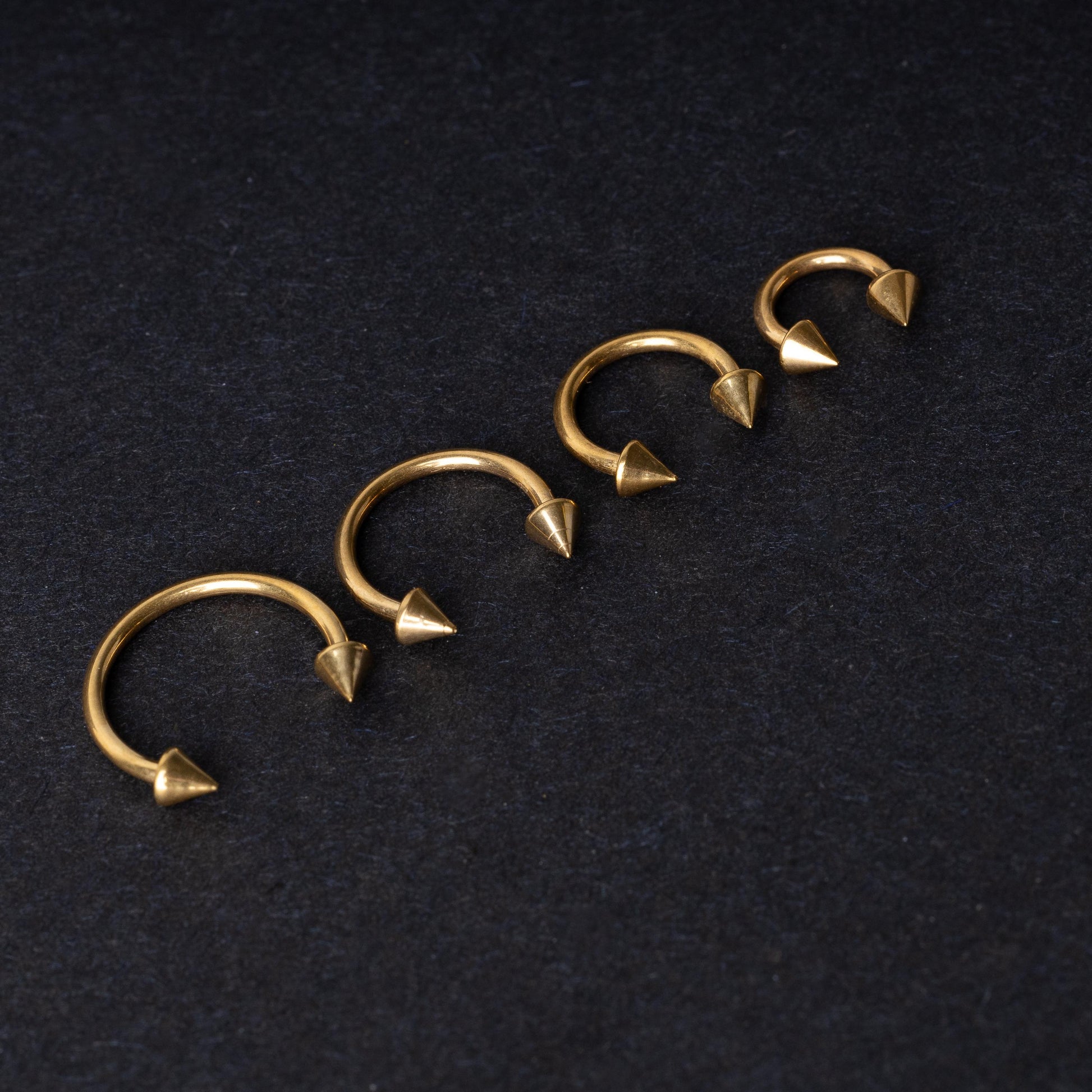 Various sized gold titanium circular barbells with spiked ends displayed on a dark background, arranged by size from large to small.