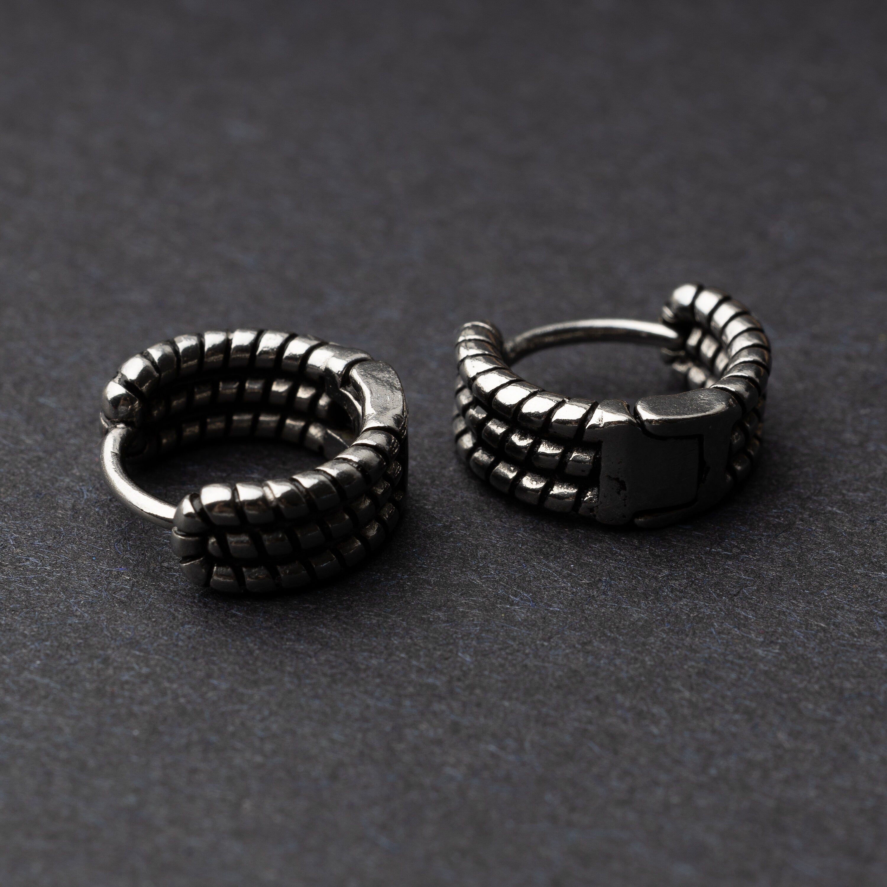 Two Silver metal hoop earrings with a bold, textured grid design, displayed on a dark background.