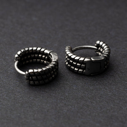 Two Silver metal hoop earrings with a bold, textured grid design, displayed on a dark background.