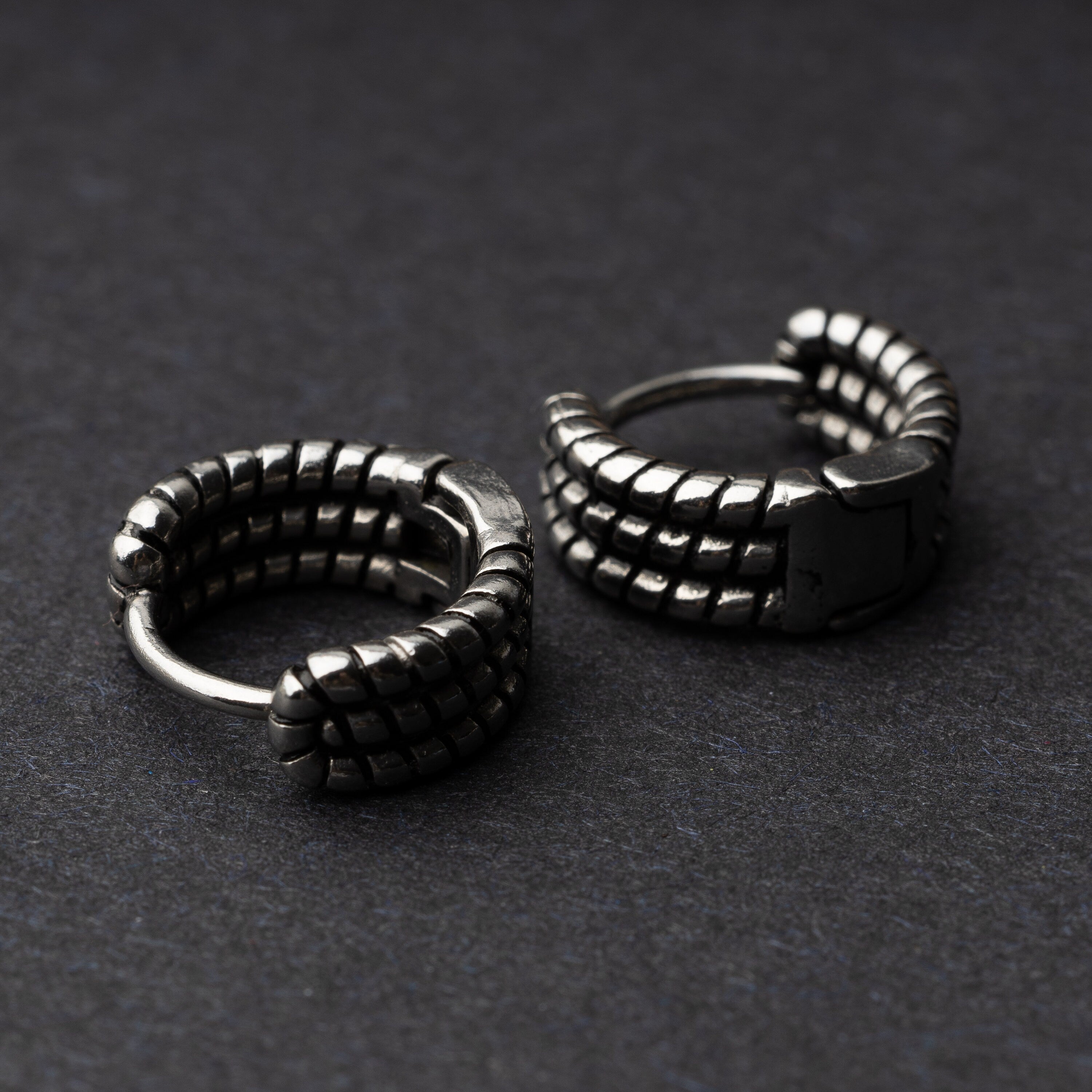 Two silver metal hoop earrings with a bold, textured grid design, displayed on a dark background.