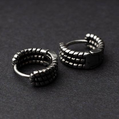 Two silver metal hoop earrings with a bold, textured grid design, displayed on a dark background.