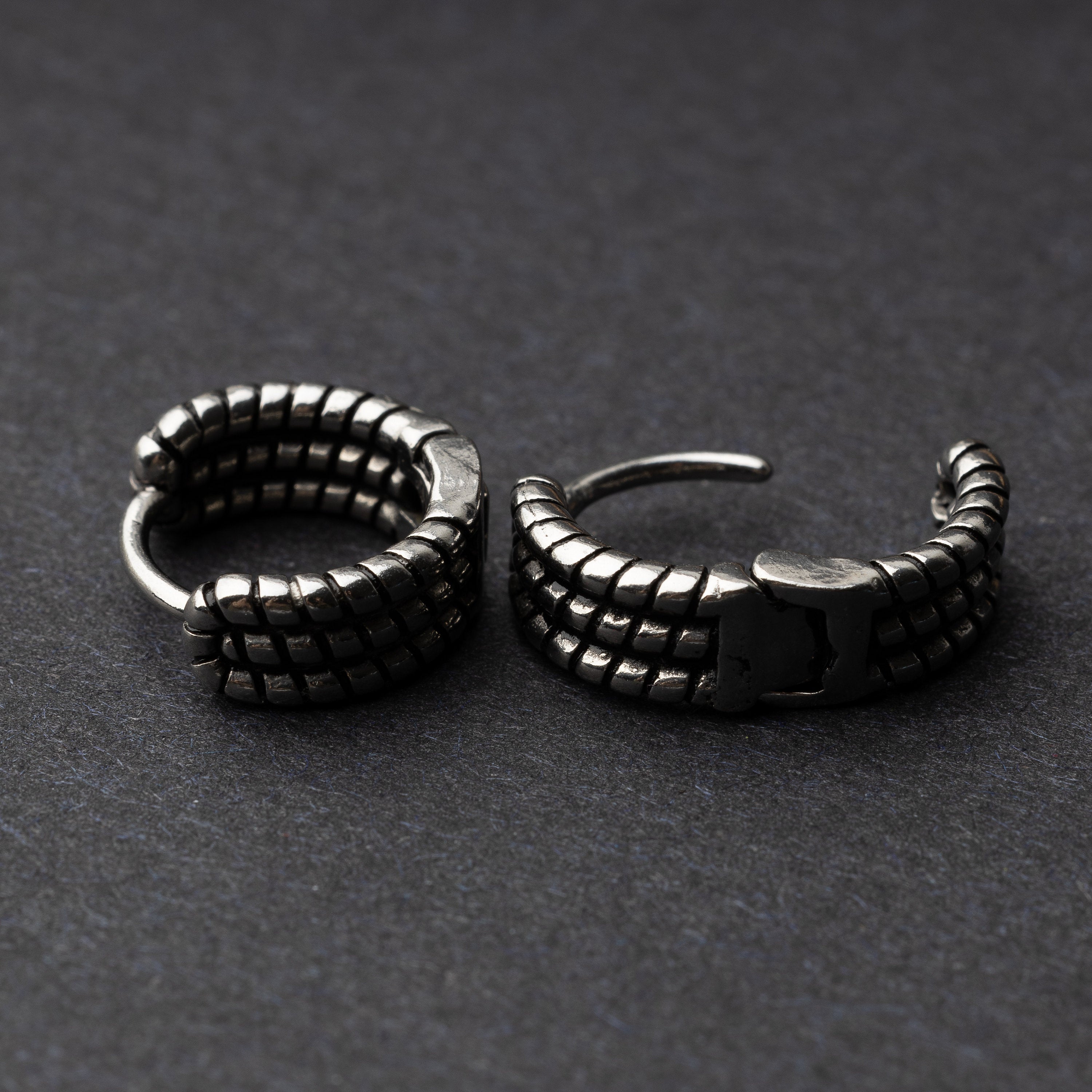 Two silver metal hoop earrings with a bold, textured grid design, displayed on a dark background.