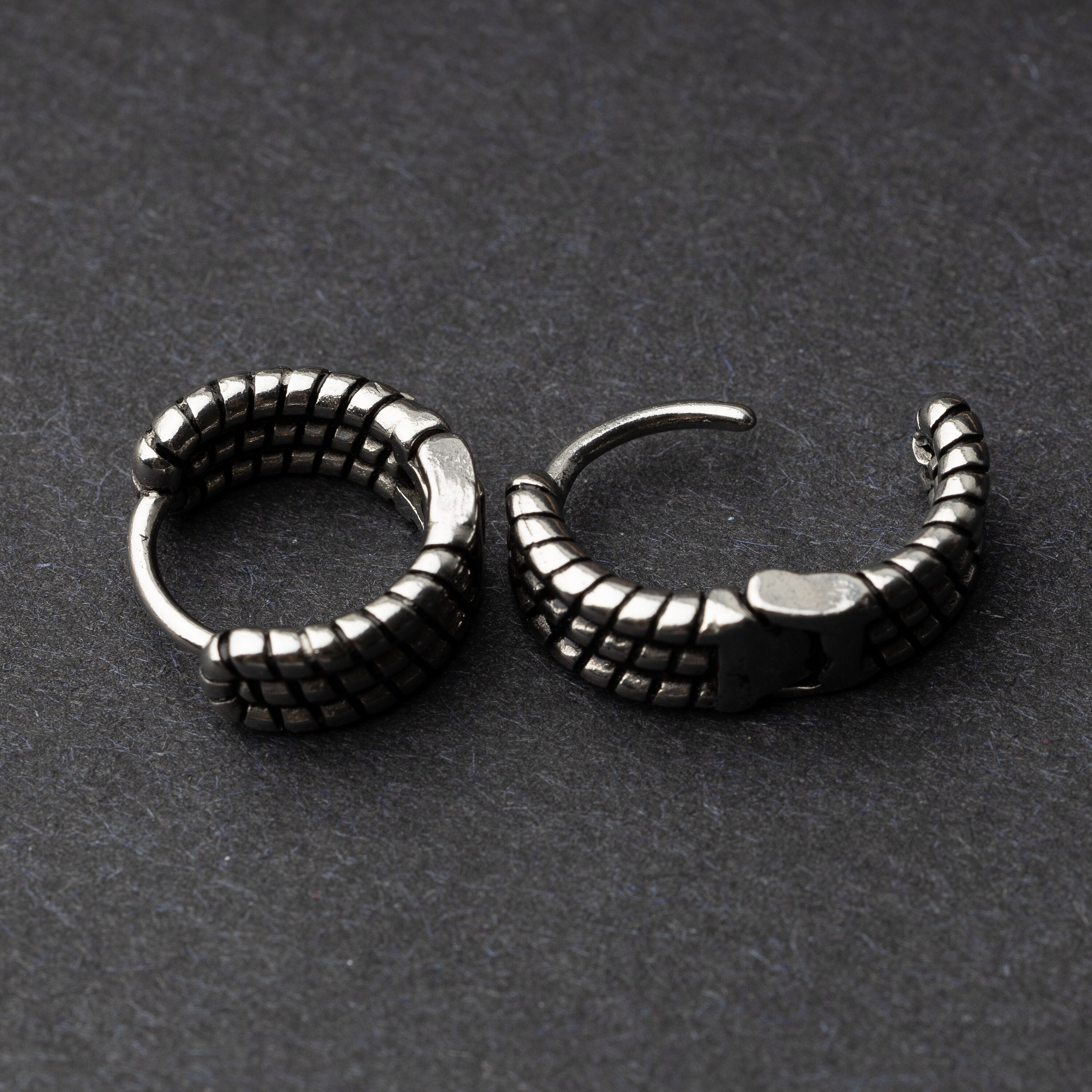 Two silver metal hoop earrings with a bold, textured grid design, displayed on a dark background.