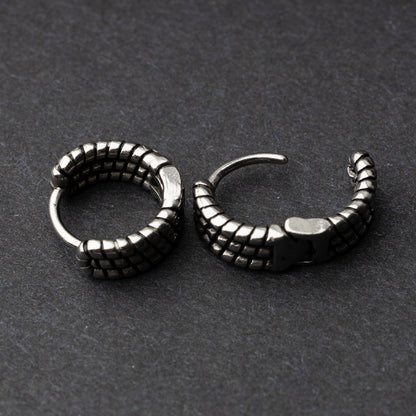 Two silver metal hoop earrings with a bold, textured grid design, displayed on a dark background.