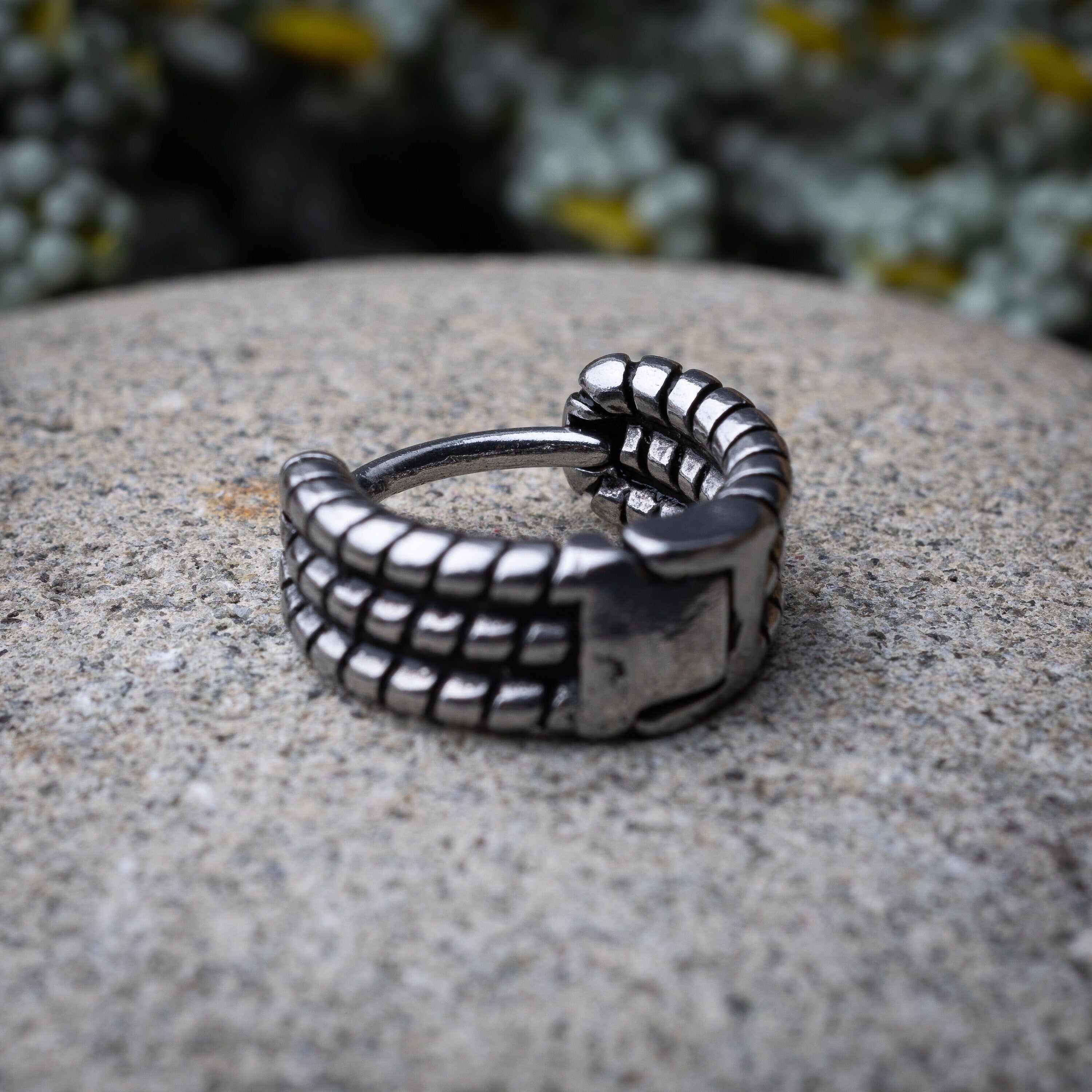 Silver metal hoop earring with a bold, textured grid design, displayed on a stone background.