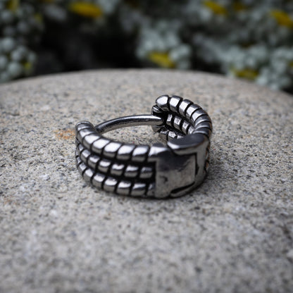 Silver metal hoop earring with a bold, textured grid design, displayed on a stone background.