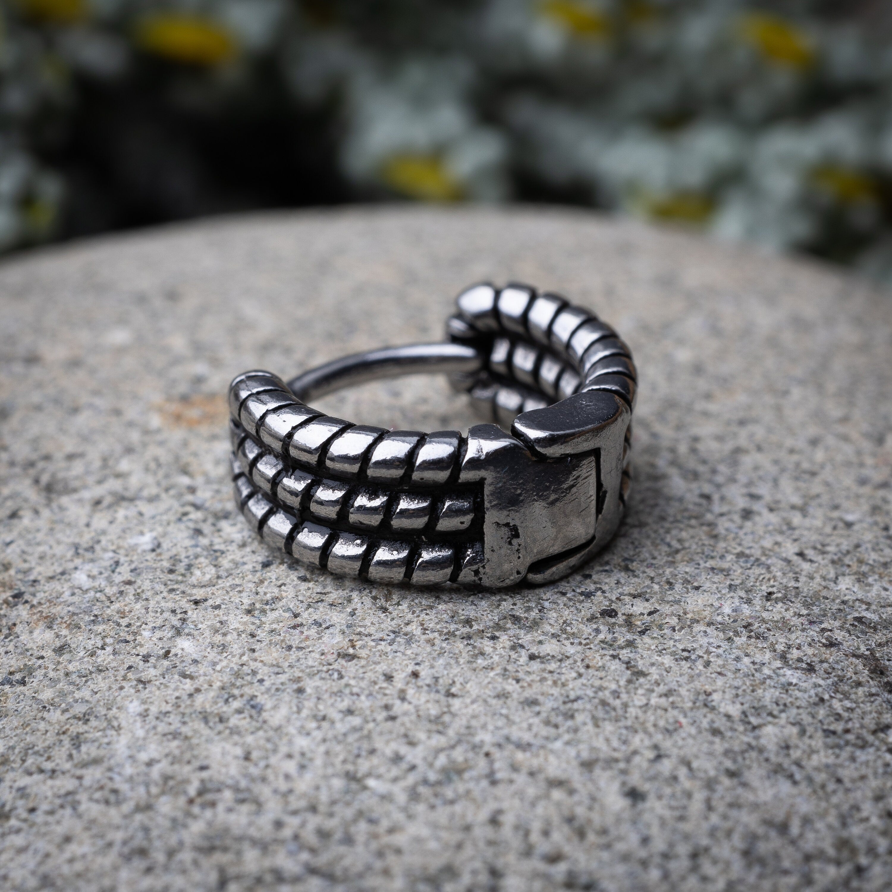 Silver metal hoop earrins with a bold, textured grid design, displayed on a stone background.