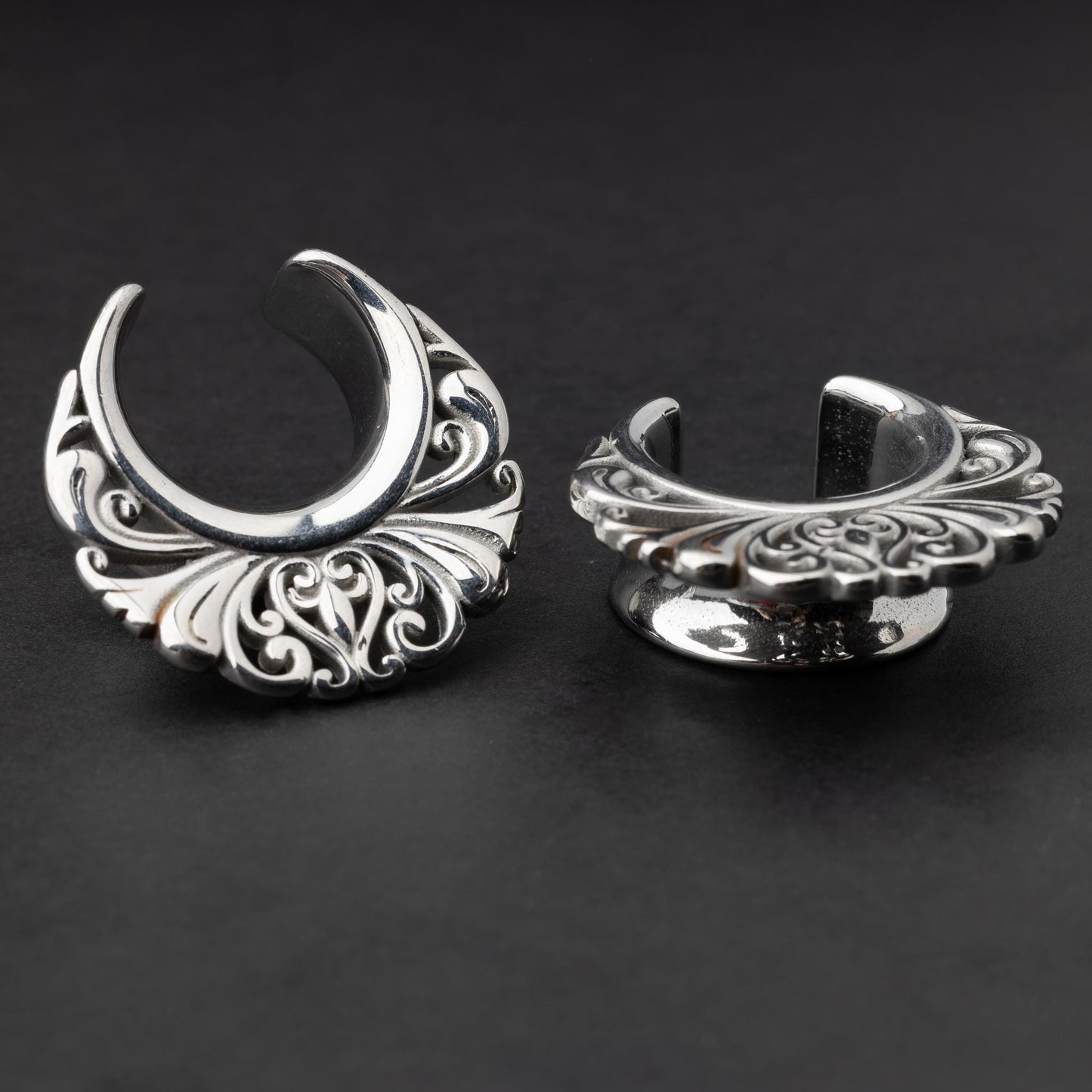 Pair of silver saddle tunnels with swirling decorative patterns for stretched ears.