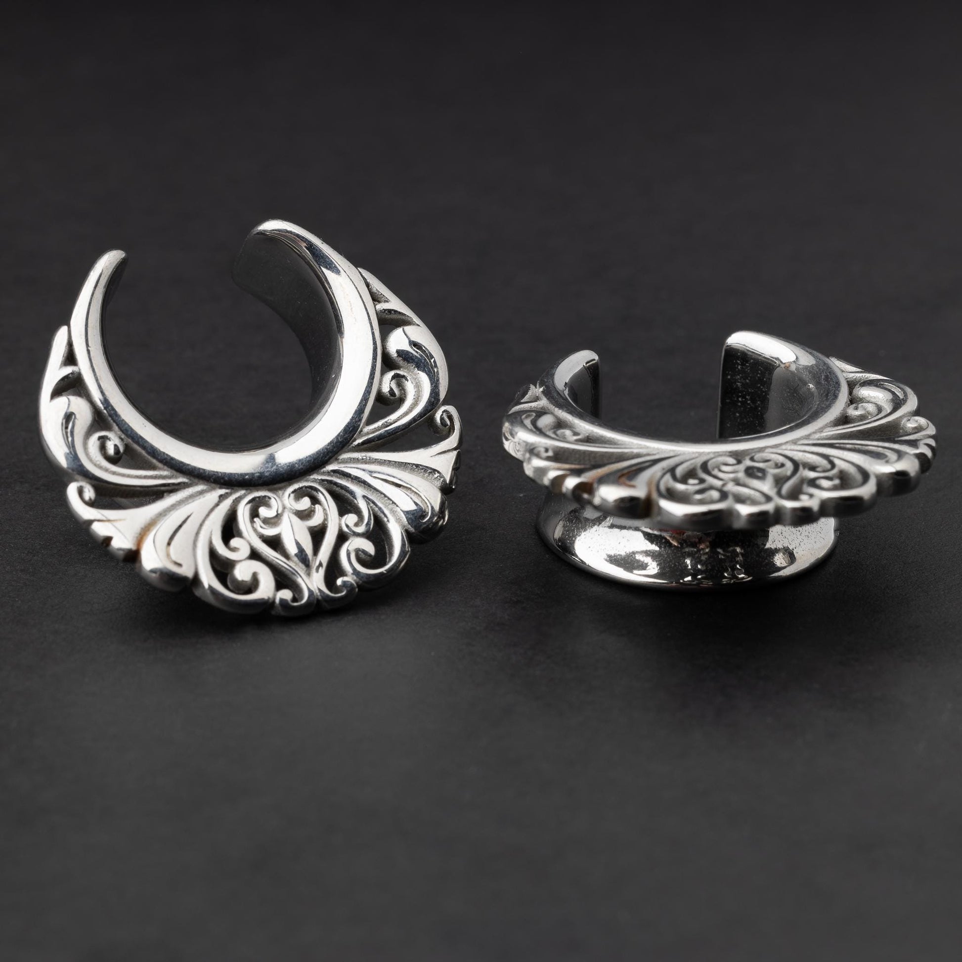 Pair of silver saddle tunnels with swirling decorative patterns for stretched ears.