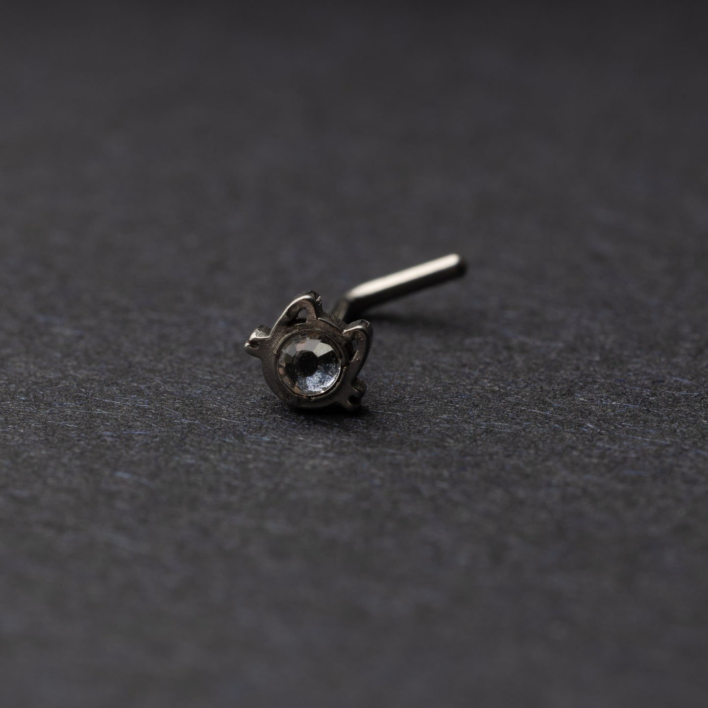 A silver stud earring in the shape of a cat’s face with a bezel-set gemstone, displayed on a dark background.