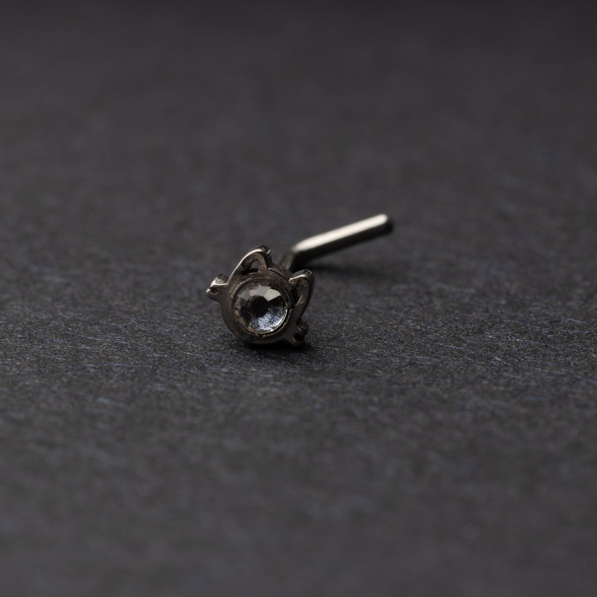 A silver stud earring in the shape of a cat’s face with a bezel-set gemstone, displayed on a dark background.