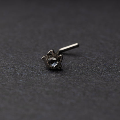 A silver stud earring in the shape of a cat’s face with a bezel-set gemstone, displayed on a dark background.