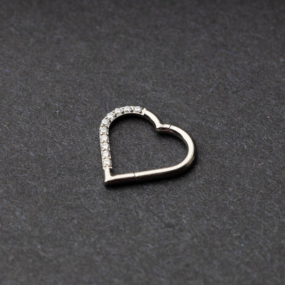 Heart-shaped daith clicker with crystal accents along one side, displayed on a dark textured background.