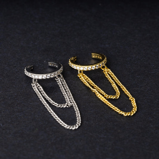 Two septum clickers with double chains and gem-encrusted arcs, one in silver and one in gold, displayed on a black background.