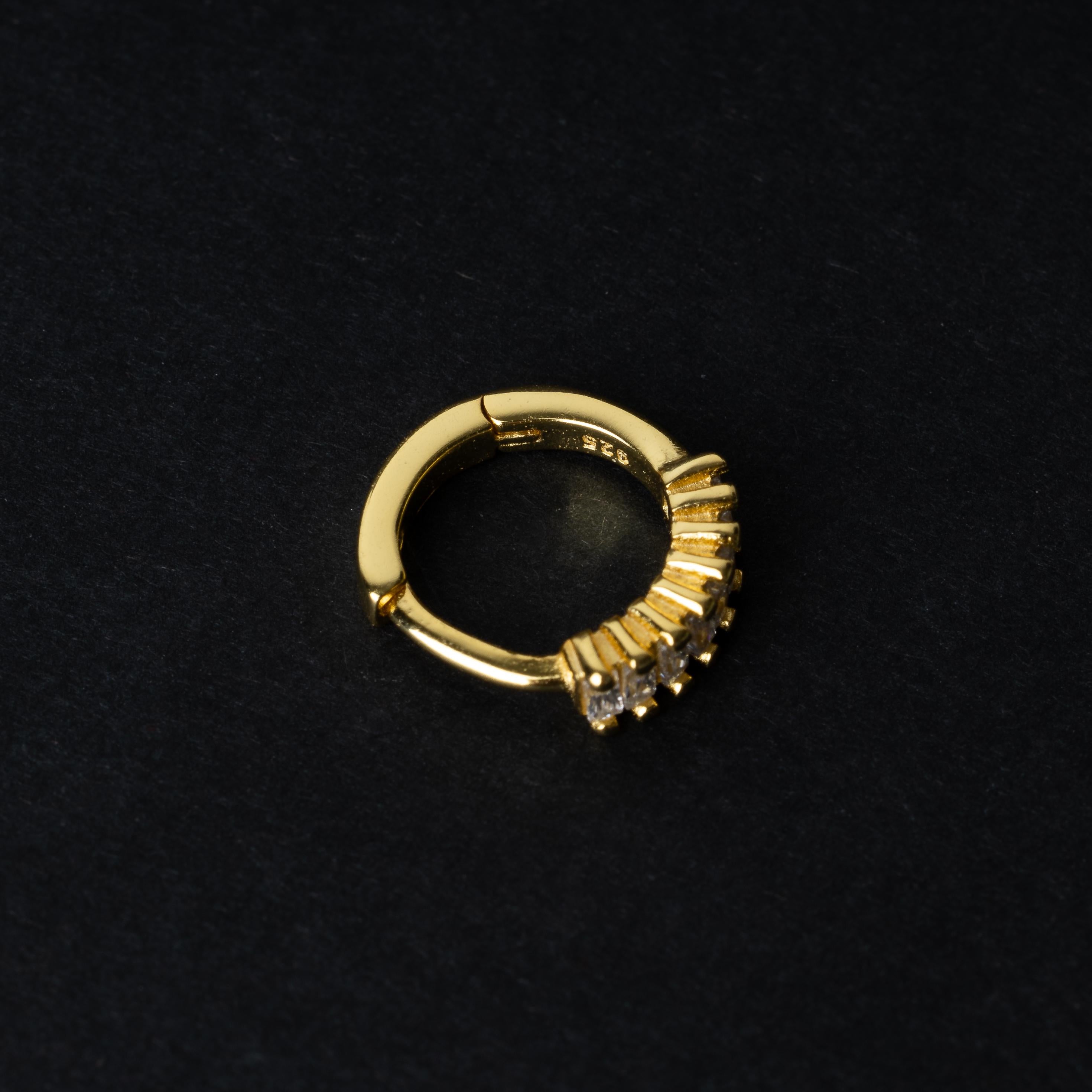 A gold septum clicker featuring a row of sparkling cubic zirconia gemstones, displayed on a black background.
