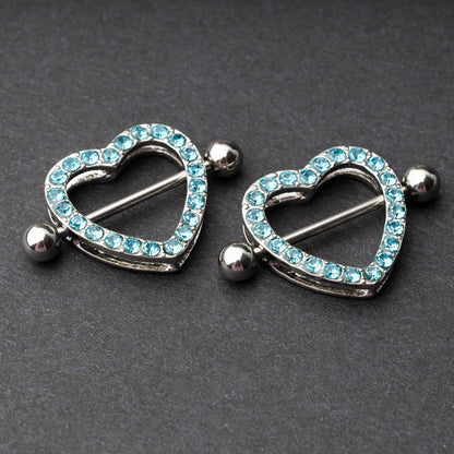 Two heart-shaped nipple barbells with silver metal and light blue gemstone accents, displayed on a dark background.