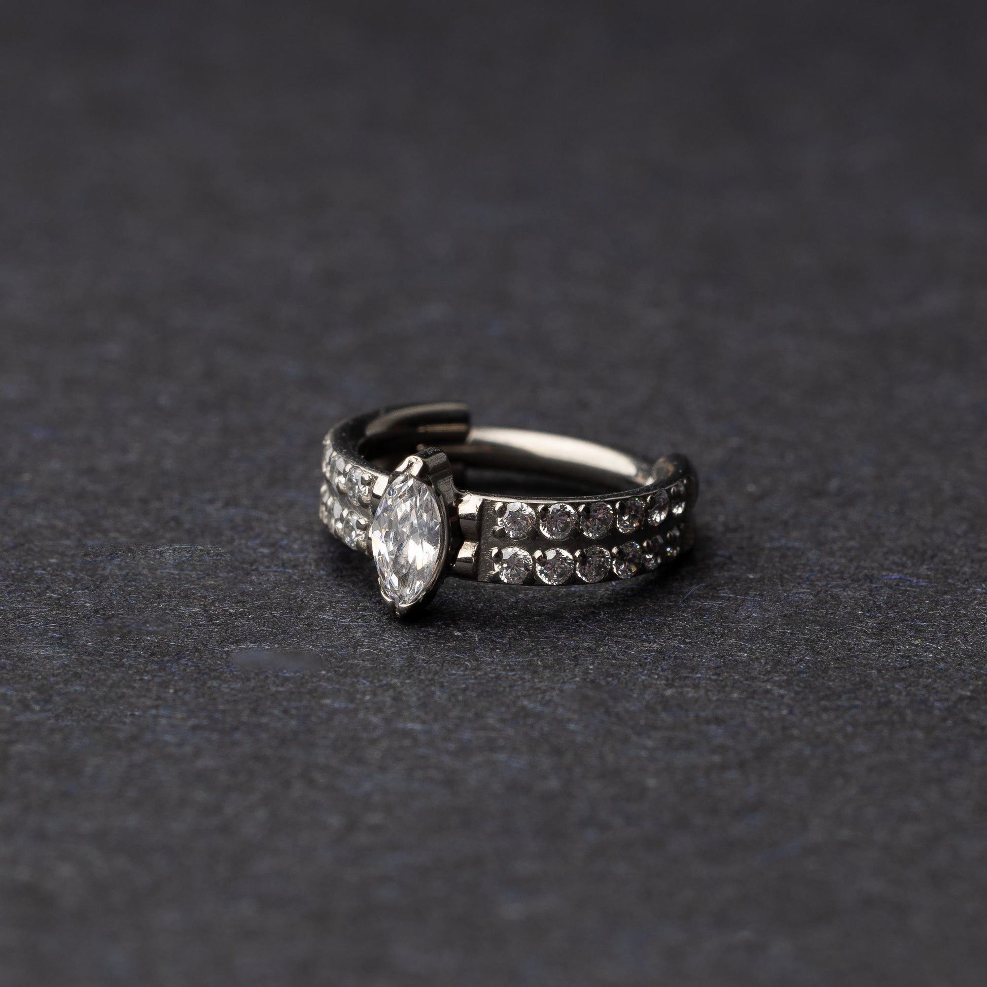 A close-up of a marquise gemstone septum or helix clicker with dual rows of sparkling gems displayed on a dark background.


