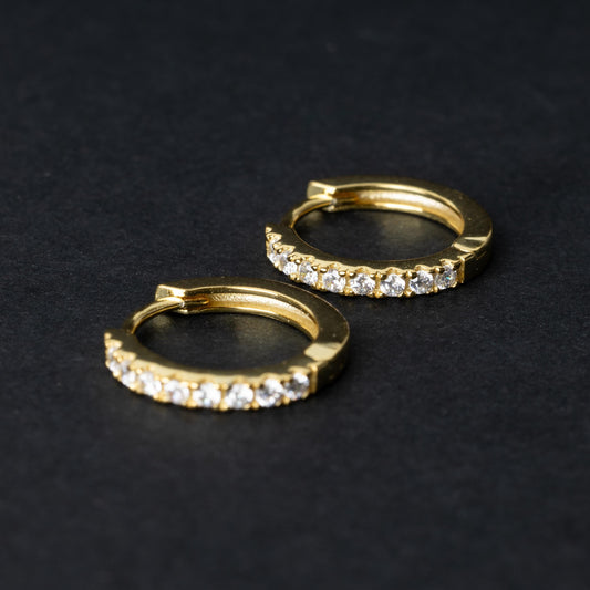 A pair of gold hoop earrings adorned with a row of sparkling cubic zirconia gems, displayed on a black background.