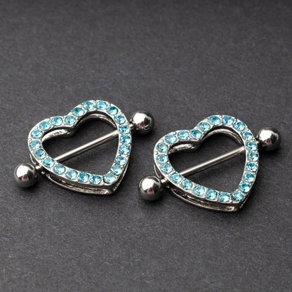 Two heart-shaped nipple barbells with silver metal and light blue gemstone accents, displayed on a dark background.